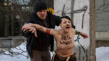 shocking-moment-topless-protester-posing-as-hitler-is-arrested-scrawling-swastikas-on-remnants-of-berlin-wall