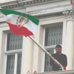 protester-scales-iranian-embassy-in-london,-tears-down-regime-flag,-hoists-pre-revolution-symbol