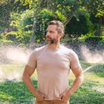 like-genghis-khan-gazing-over-his-empire,-man-watches-as-fixed-sprinkler-no-longer-waters-driveway