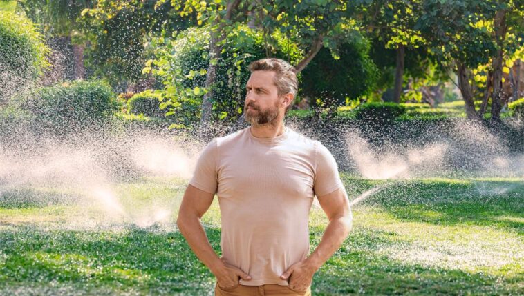 like-genghis-khan-gazing-over-his-empire,-man-watches-as-fixed-sprinkler-no-longer-waters-driveway
